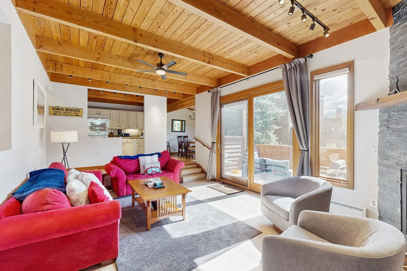 A bright living room with colorful seating, large windows, and an exposed wood ceiling.