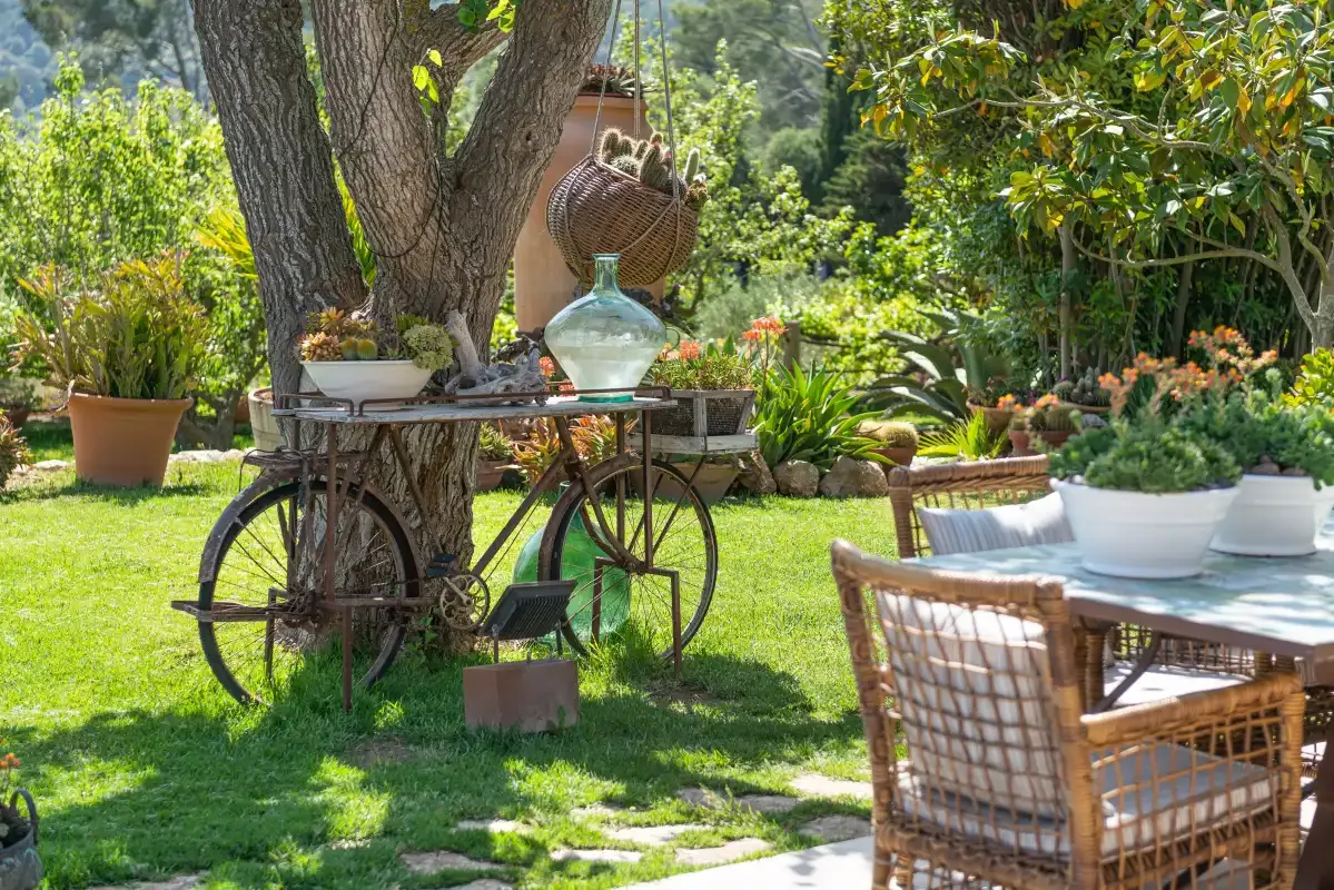A garden dining area with a table and chairs beneath leafy trees.