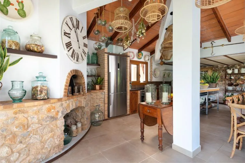 A rustic kitchen with a stone counter, hanging baskets, and a stainless steel refrigerator.