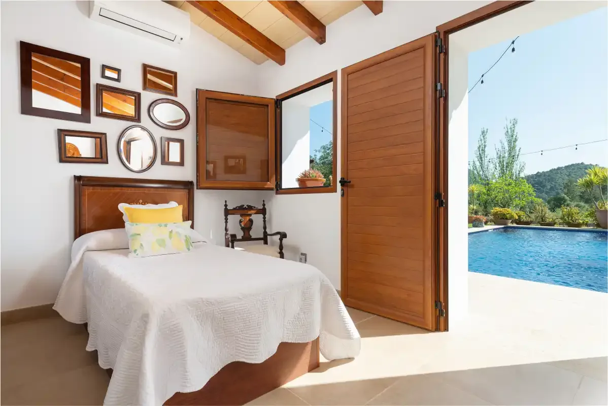 A bedroom with a bed beside an open wooden door overlooking a pool.