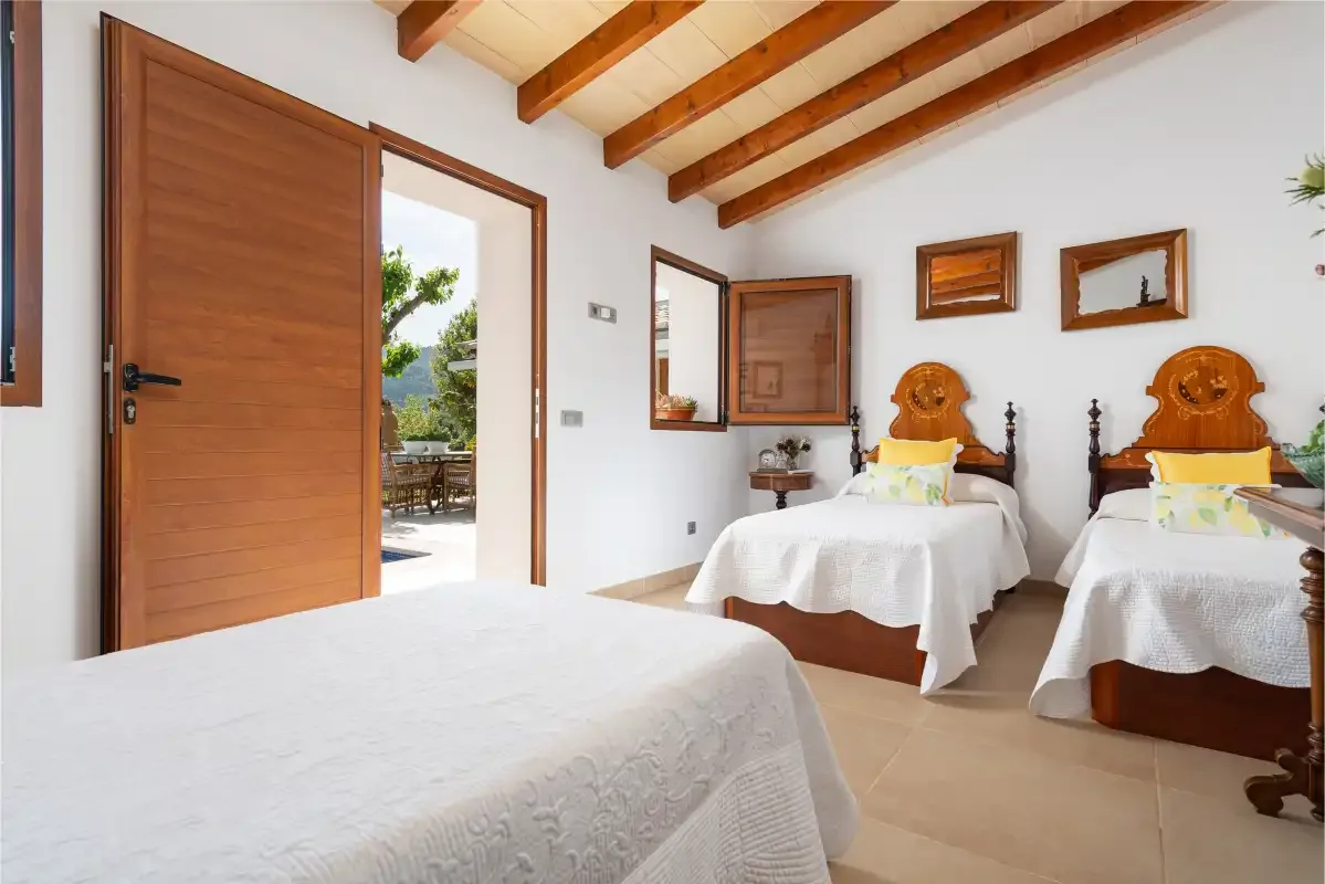 A bedroom with three beds, including two twin beds beneath exposed wooden ceiling beams.