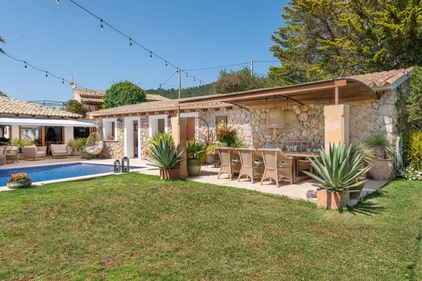 A stone patio with outdoor seating overlooks a swimming pool and grassy yard.