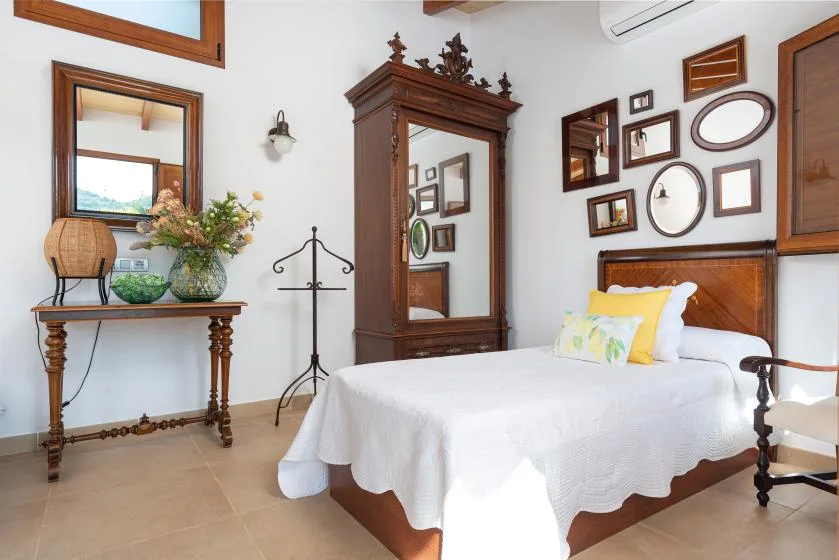A bedroom with a white-covered bed, wooden wardrobe, and wall mirrors.