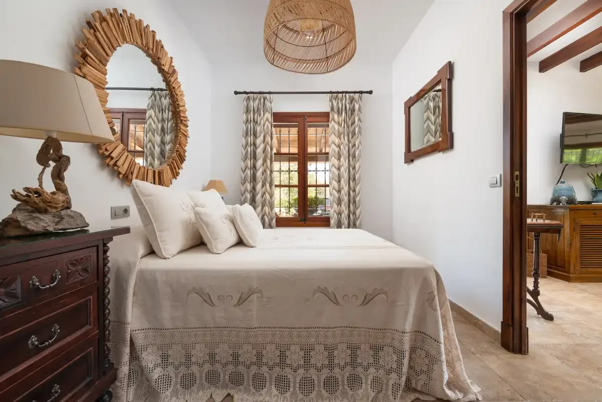 A bedroom with a neatly made bed and a curtained window.