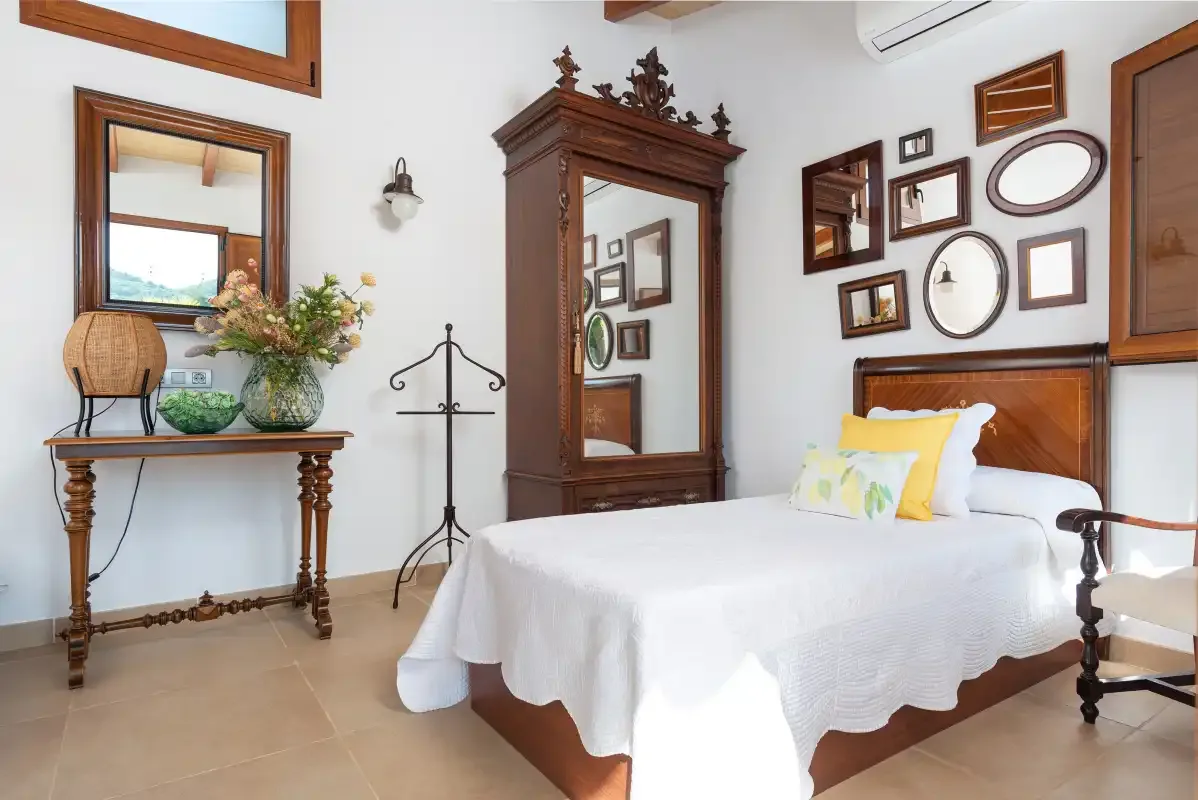 A bedroom with a white-covered bed and framed mirrors on the wall.