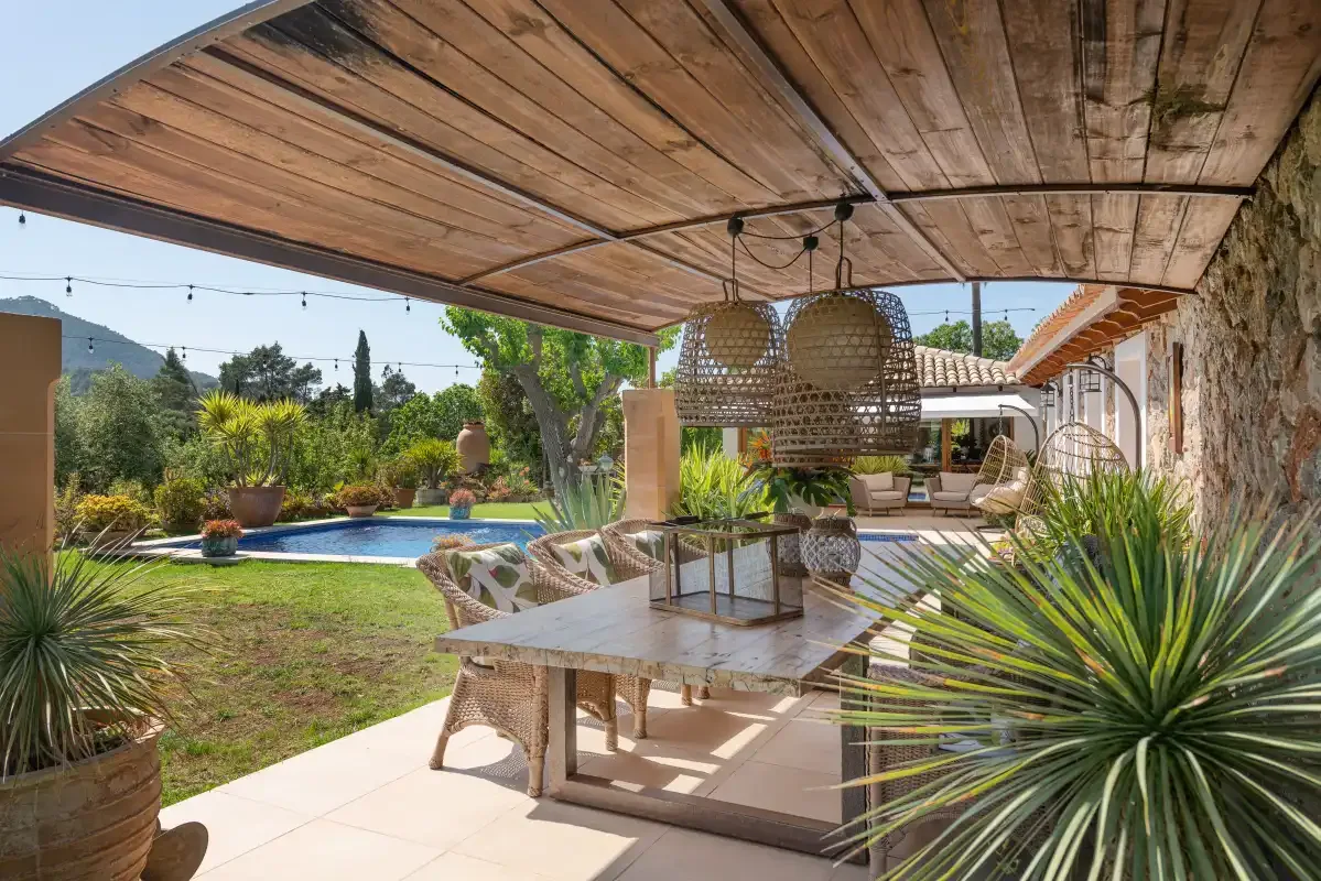 A covered outdoor dining area overlooks a garden and swimming pool.
