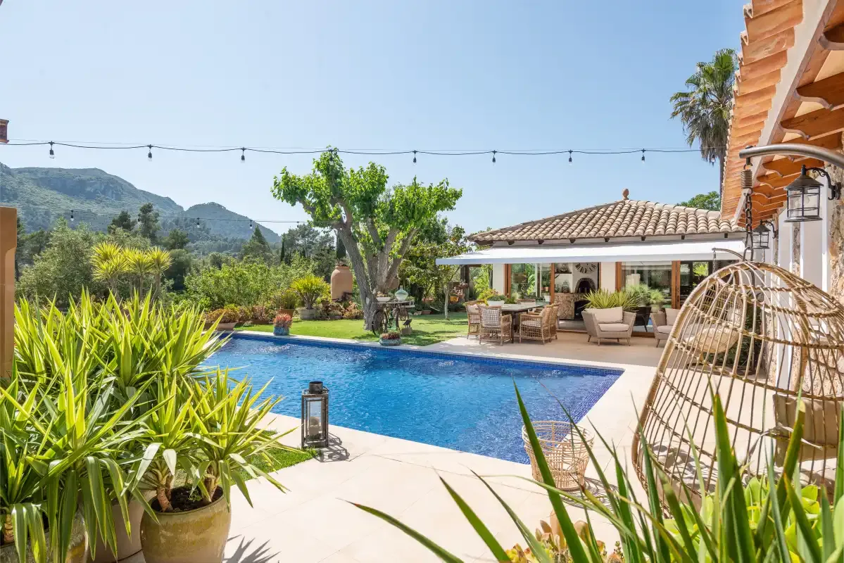 An outdoor pool beside a covered patio, surrounded by greenery.