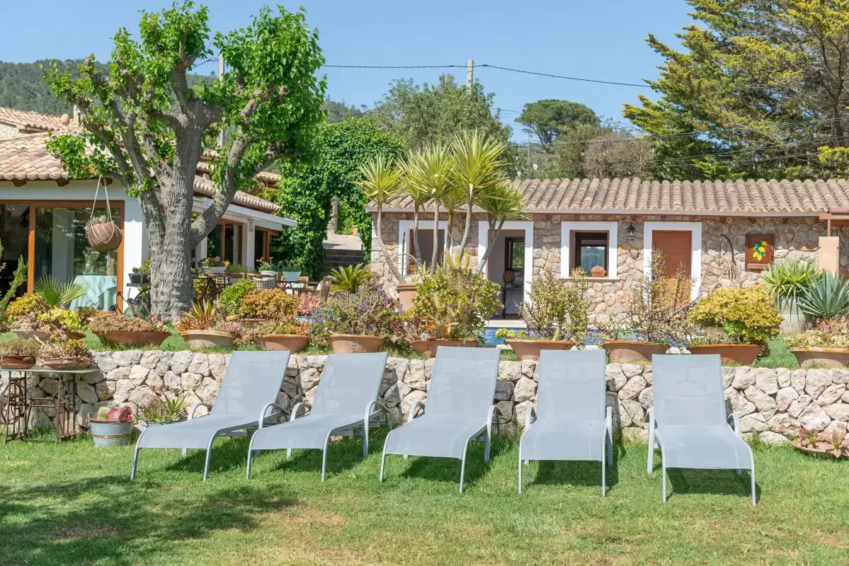 A stone house and garden with several lounge chairs on the lawn.