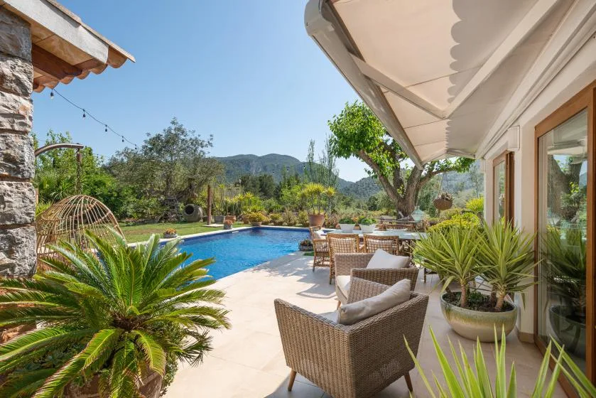 A sunny poolside patio with outdoor seating and potted plants.
