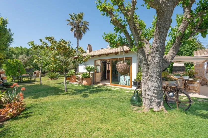 A garden patio beside a small house, with a large tree shading outdoor seating.