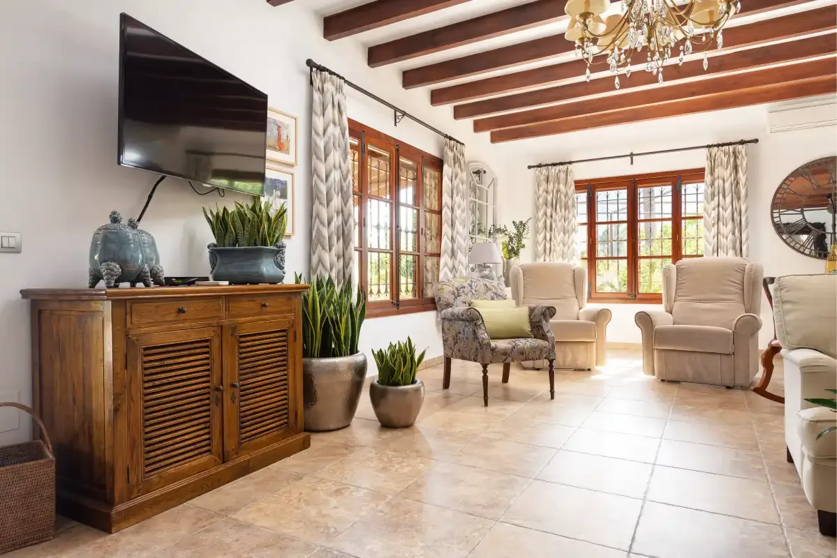 A bright living room has cushioned seating, large windows, and exposed ceiling beams.
