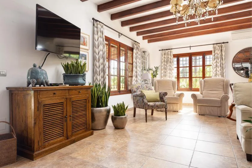 A bright living room with armchairs, a television, and exposed ceiling beams.