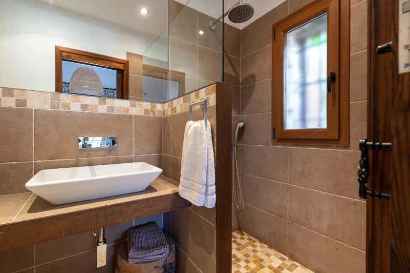 A tiled bathroom with a sink, shower, and frosted window.