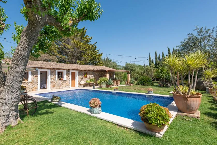 A swimming pool and landscaped garden sit beside a low stone building.