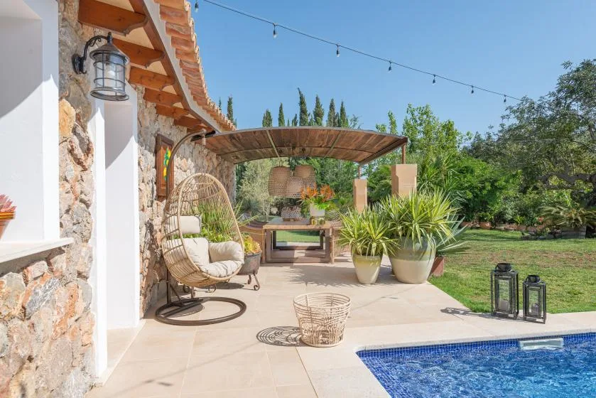 An outdoor patio with a covered seating area, potted plants, and a swimming pool.