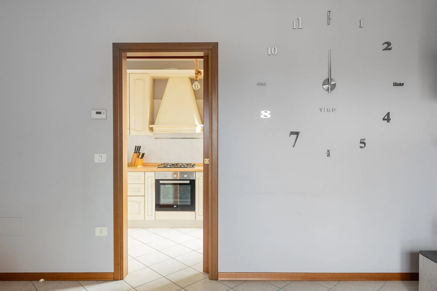 Una puerta da a una cocina luminosa, junto a un reloj minimalista en la pared.