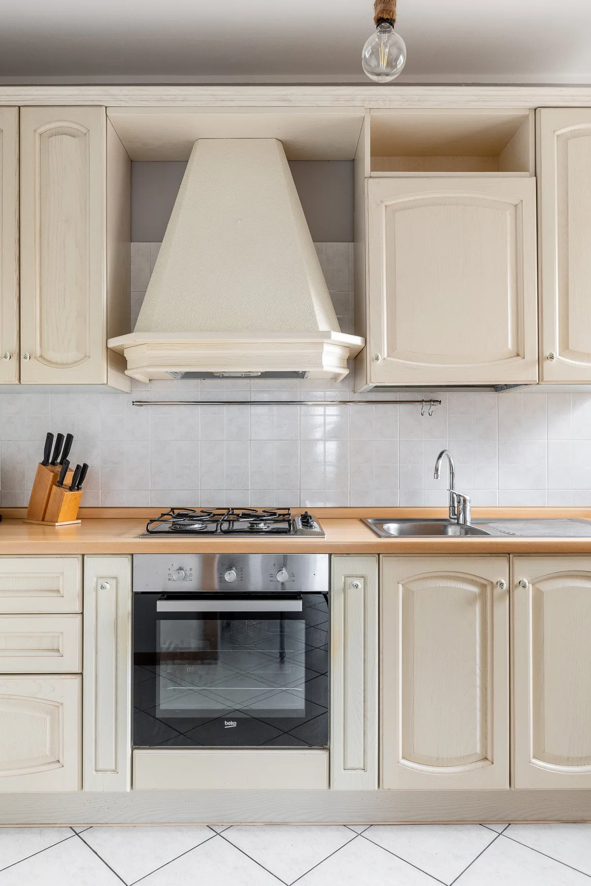 Una cocina luminosa con gabinetes color crema, campana extractora y horno empotrado.