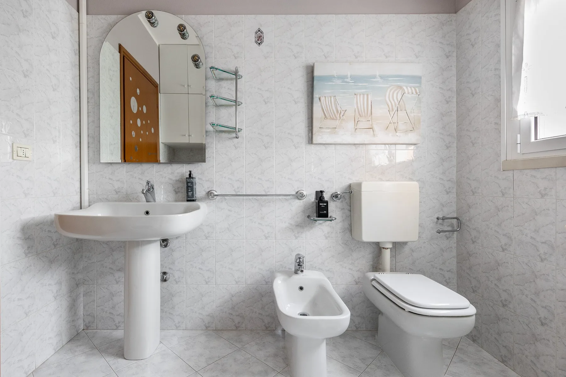 Un baño luminoso con azulejos, lavabo, inodoro y bidé.