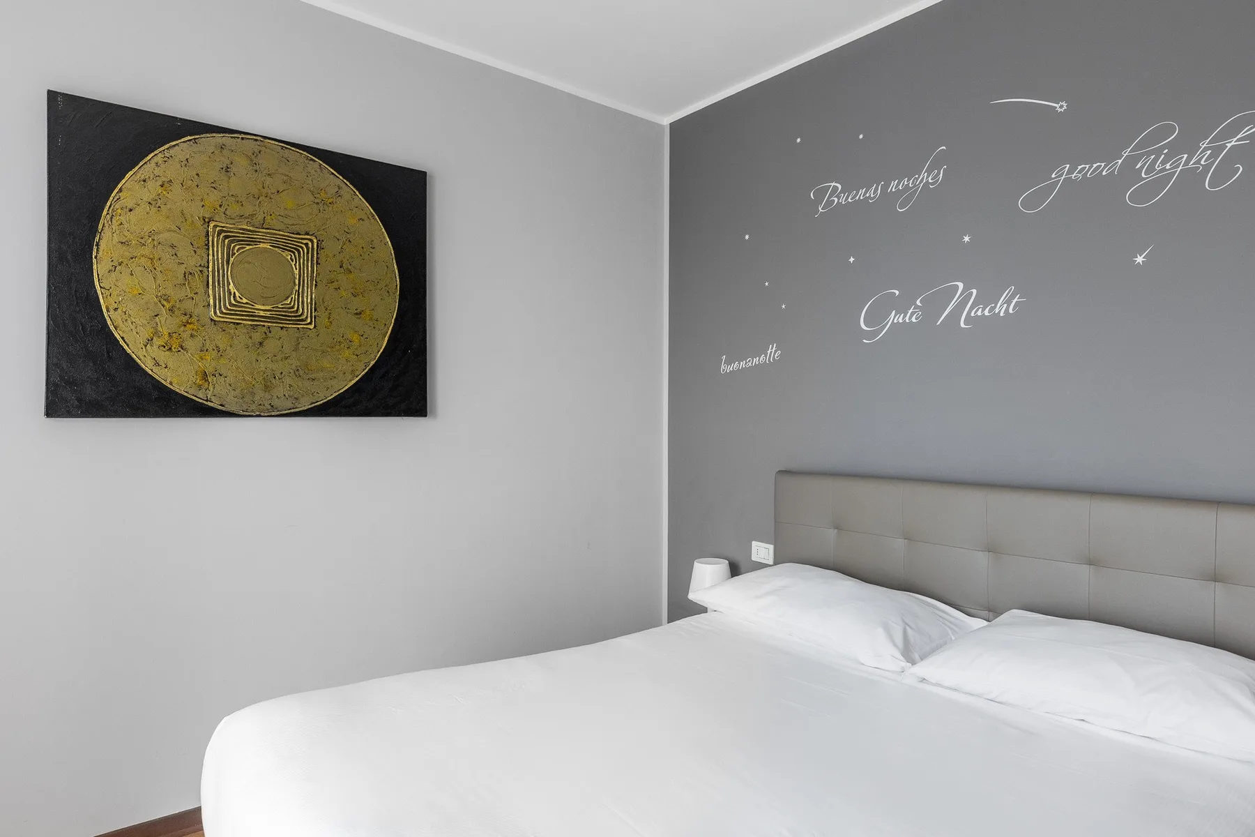 Un dormitorio con una cama bien tendida y escritura decorativa en la pared.
