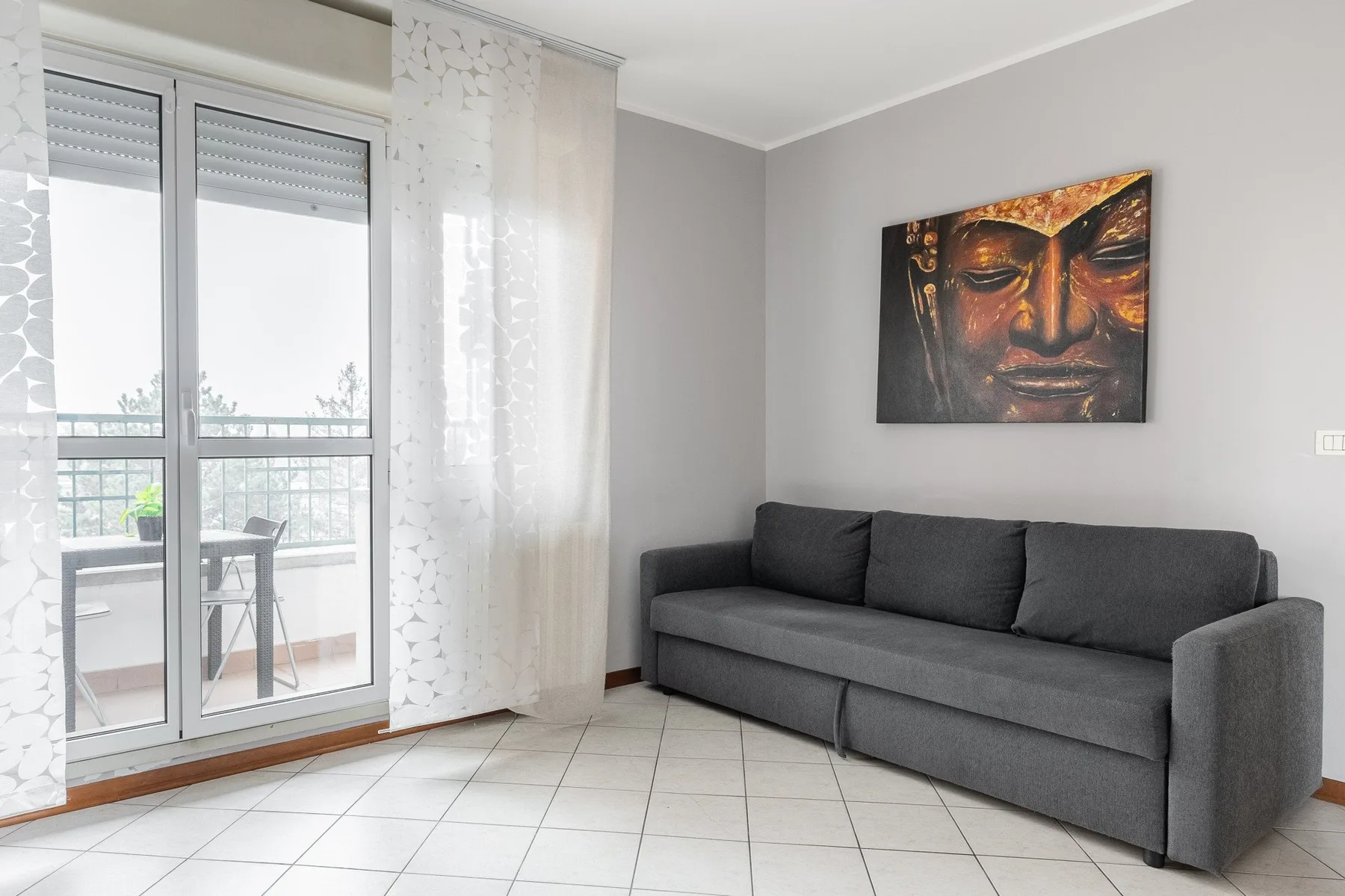 A living room with a gray sofa, a glass balcony door, and wall art.
