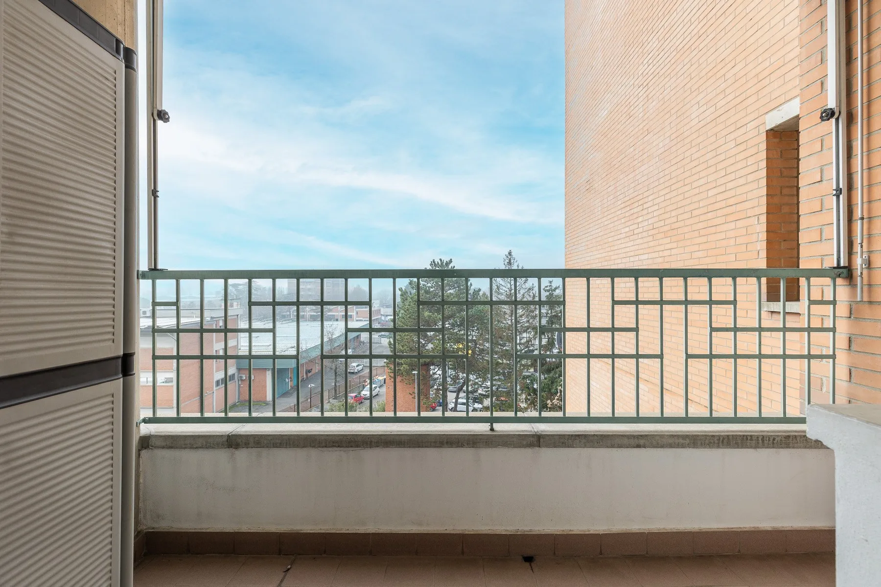 Un balcón con barandilla metálica da a edificios cercanos y árboles.