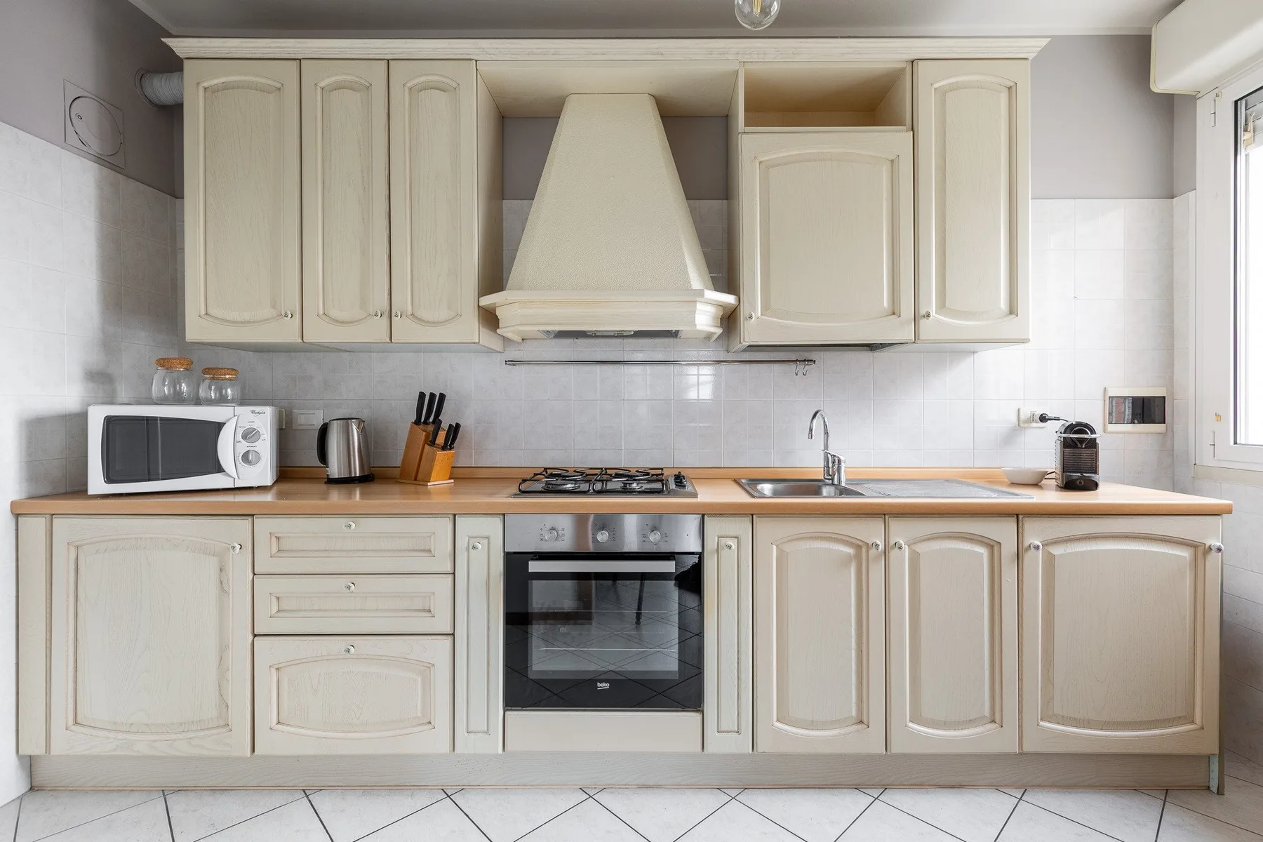 Una cocina luminosa con gabinetes color crema, una estufa y un horno empotrado.