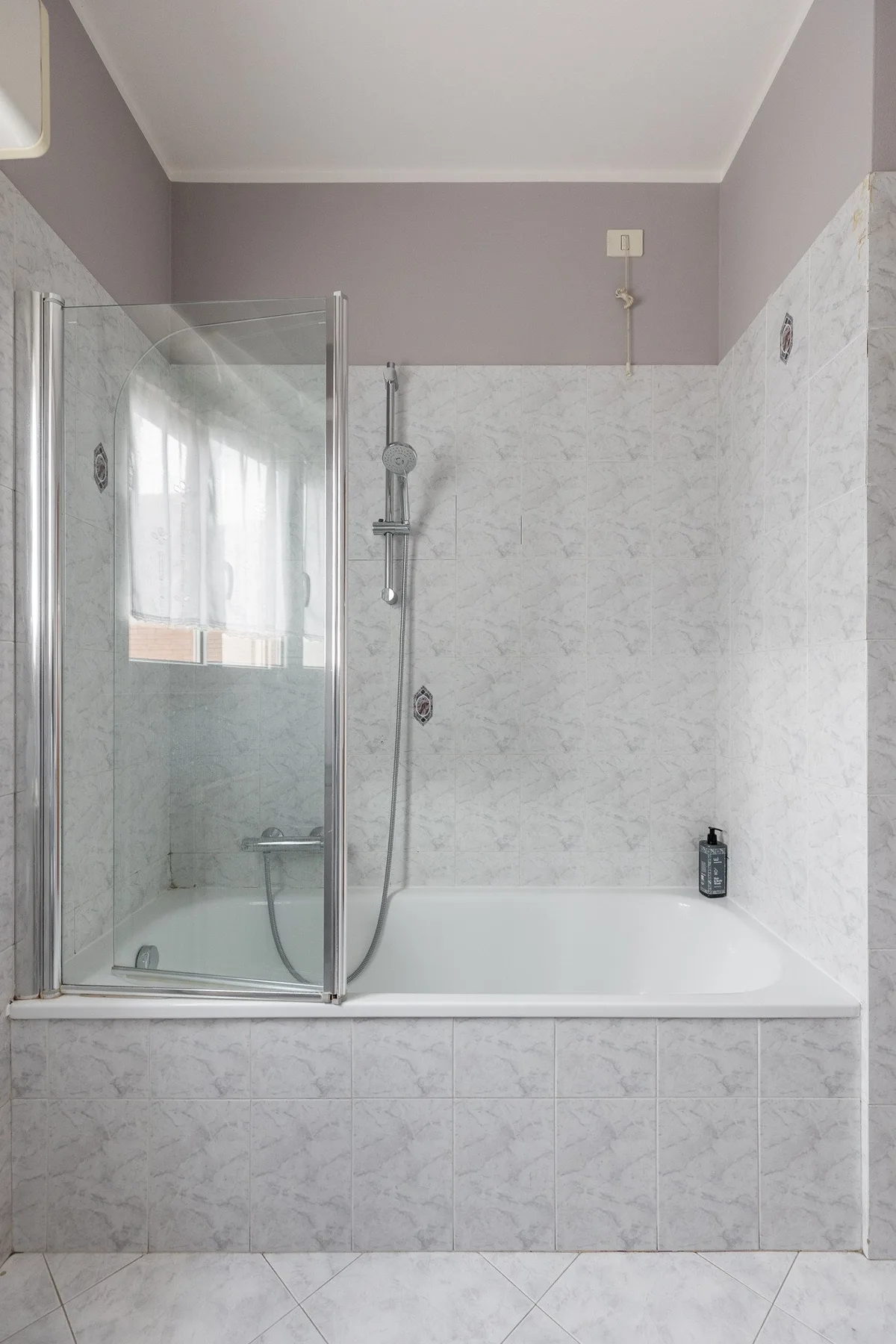 Un baño alicatado con bañera, ducha y mampara de vidrio.
