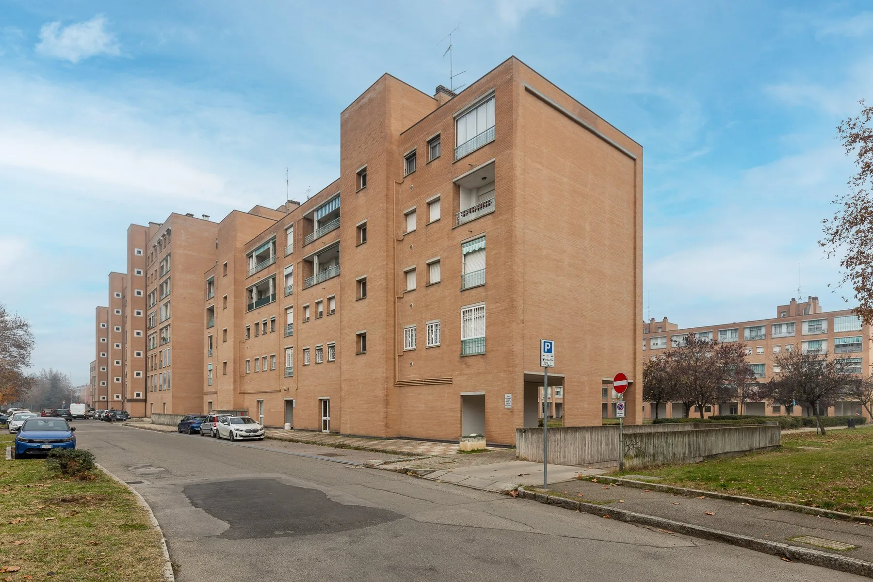 Un edificio de apartamentos de ladrillo se alza junto a una calle pavimentada y una franja de césped.