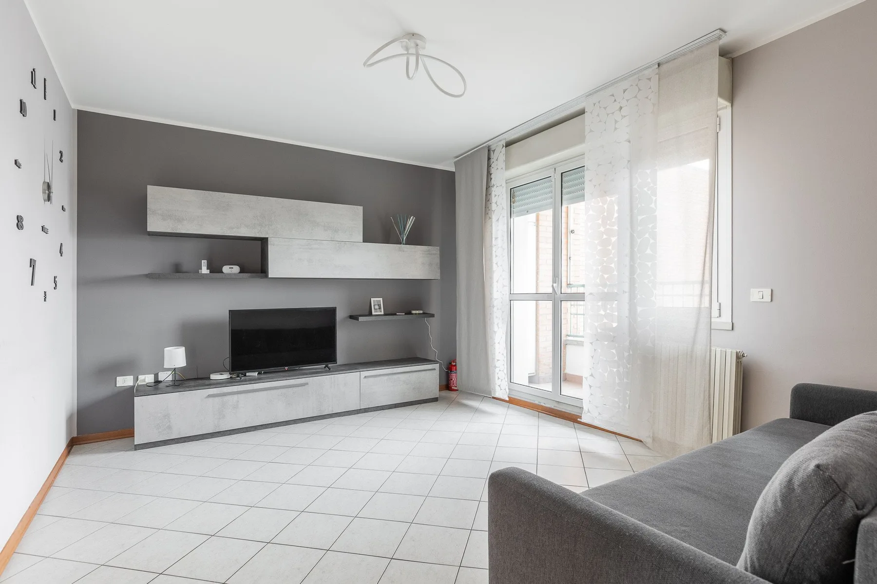 Una sala de estar moderna con televisor, muebles bajos y asientos junto a ventanas altas.