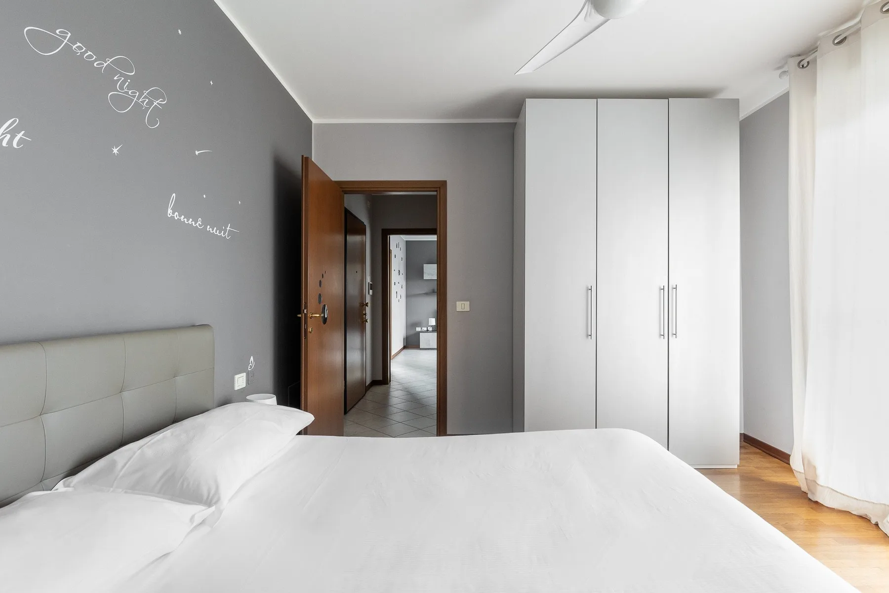 Un dormitorio luminoso con una cama bien hecha y un armario alto blanco.