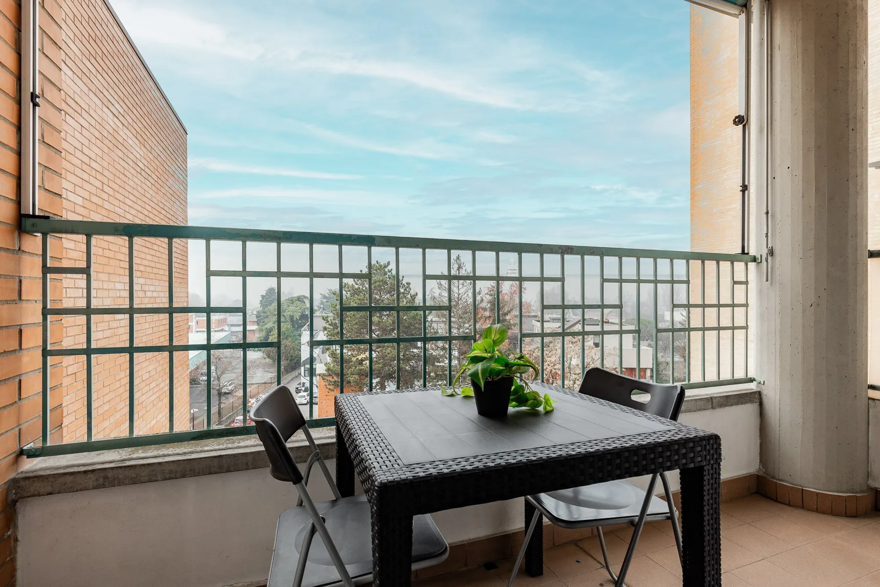 A balcony seating area with a dark table and potted plant overlooking nearby buildings.
