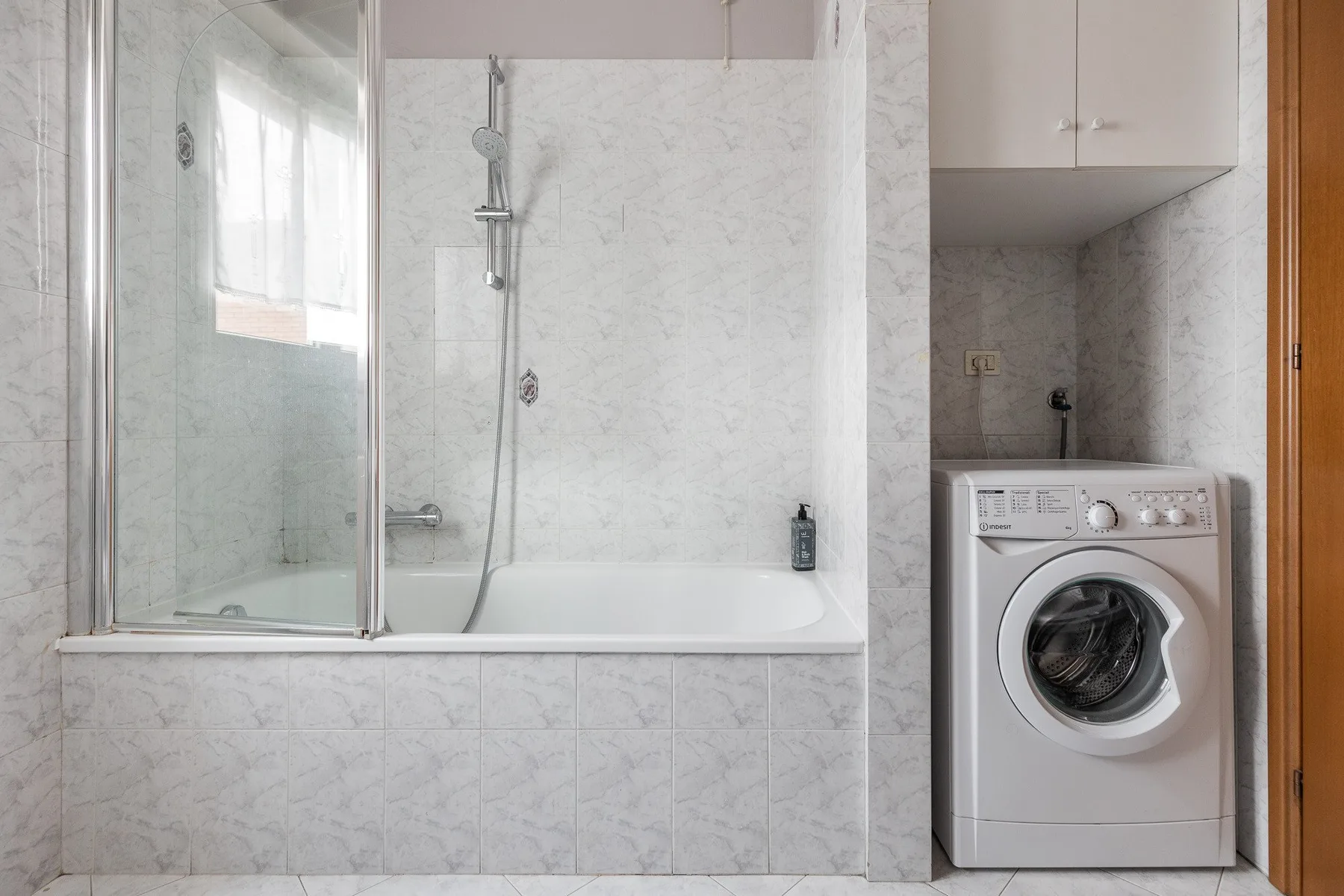 Un baño con bañera y ducha junto a una lavadora.