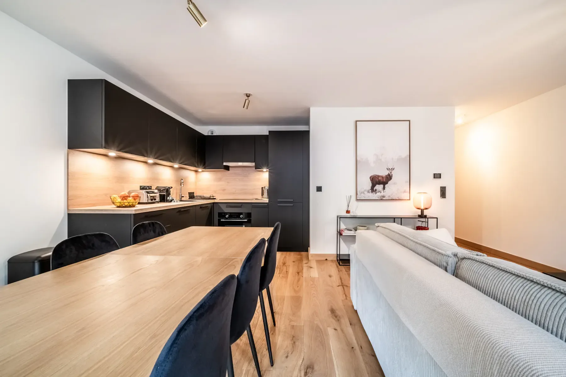 An open-plan living and dining area with a long wooden table and dark seating.
