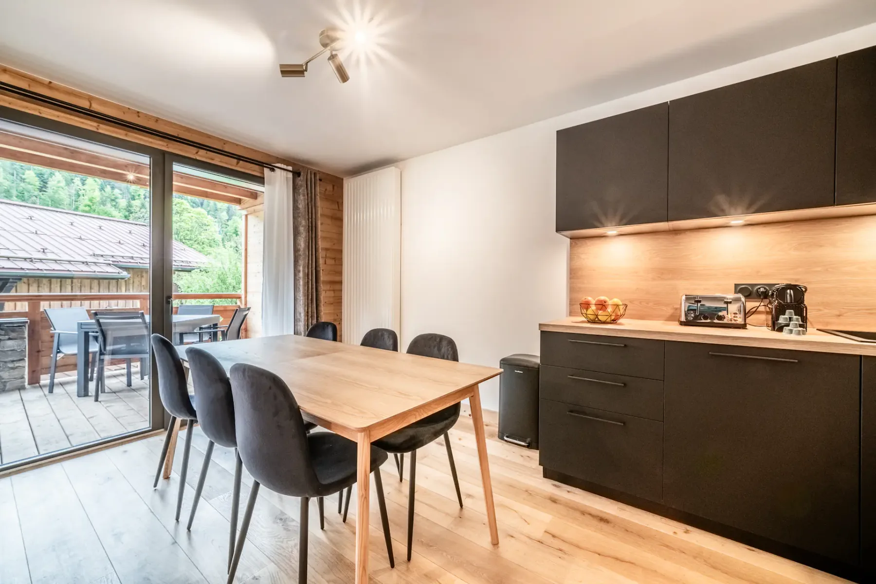 A dining area with dark cabinetry and a wooden table beside sliding glass doors opening onto a deck.