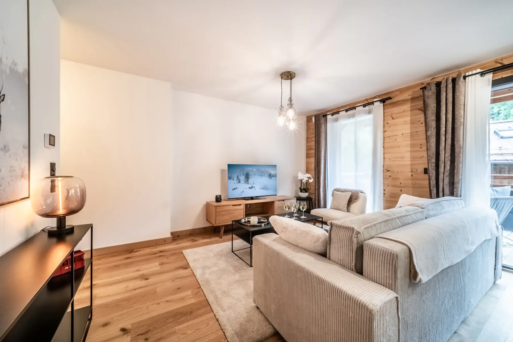 A living room with light-colored seating, a television, and a wood-paneled wall.