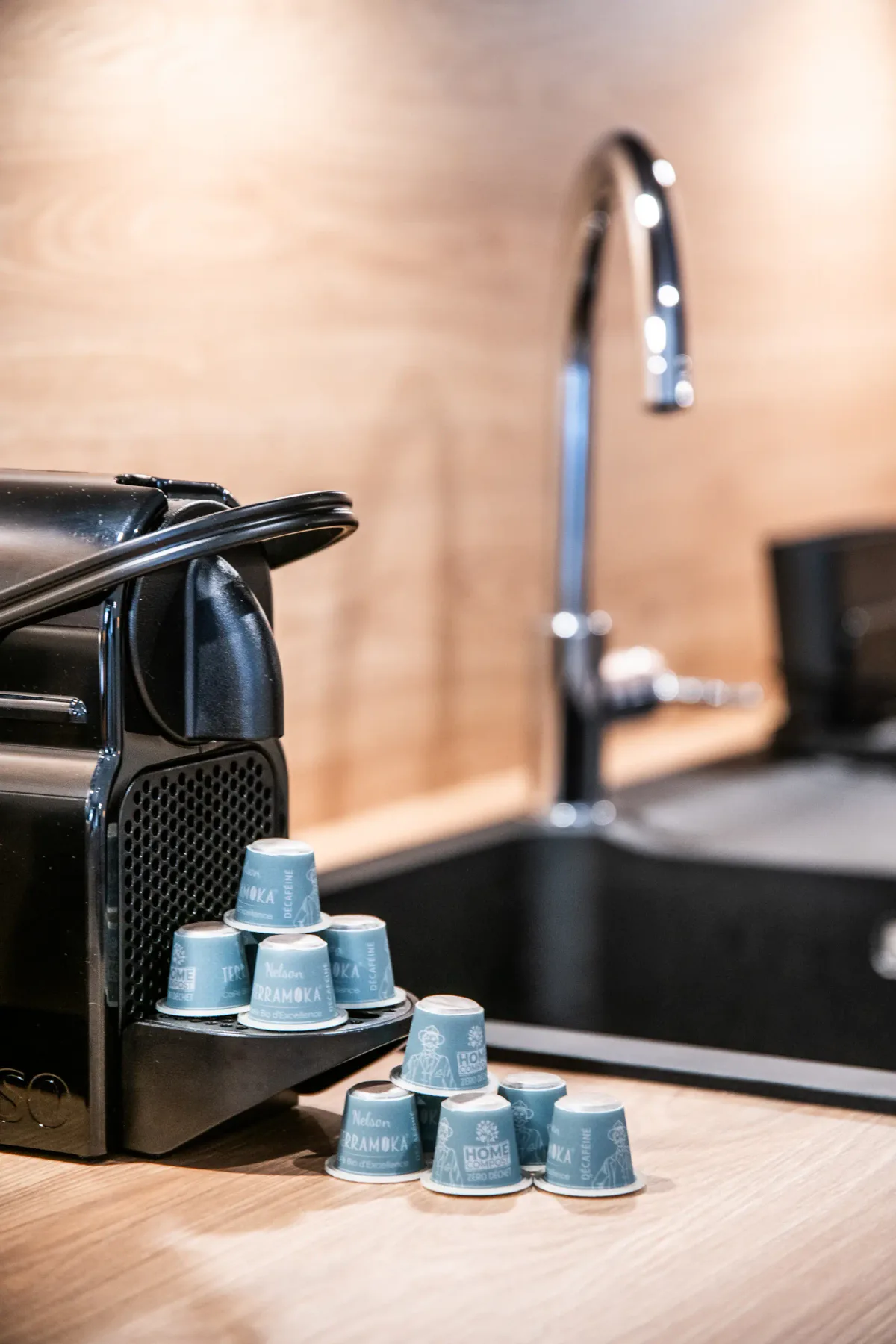 A black coffee machine sits on a countertop with a stack of blue coffee pods labeled
