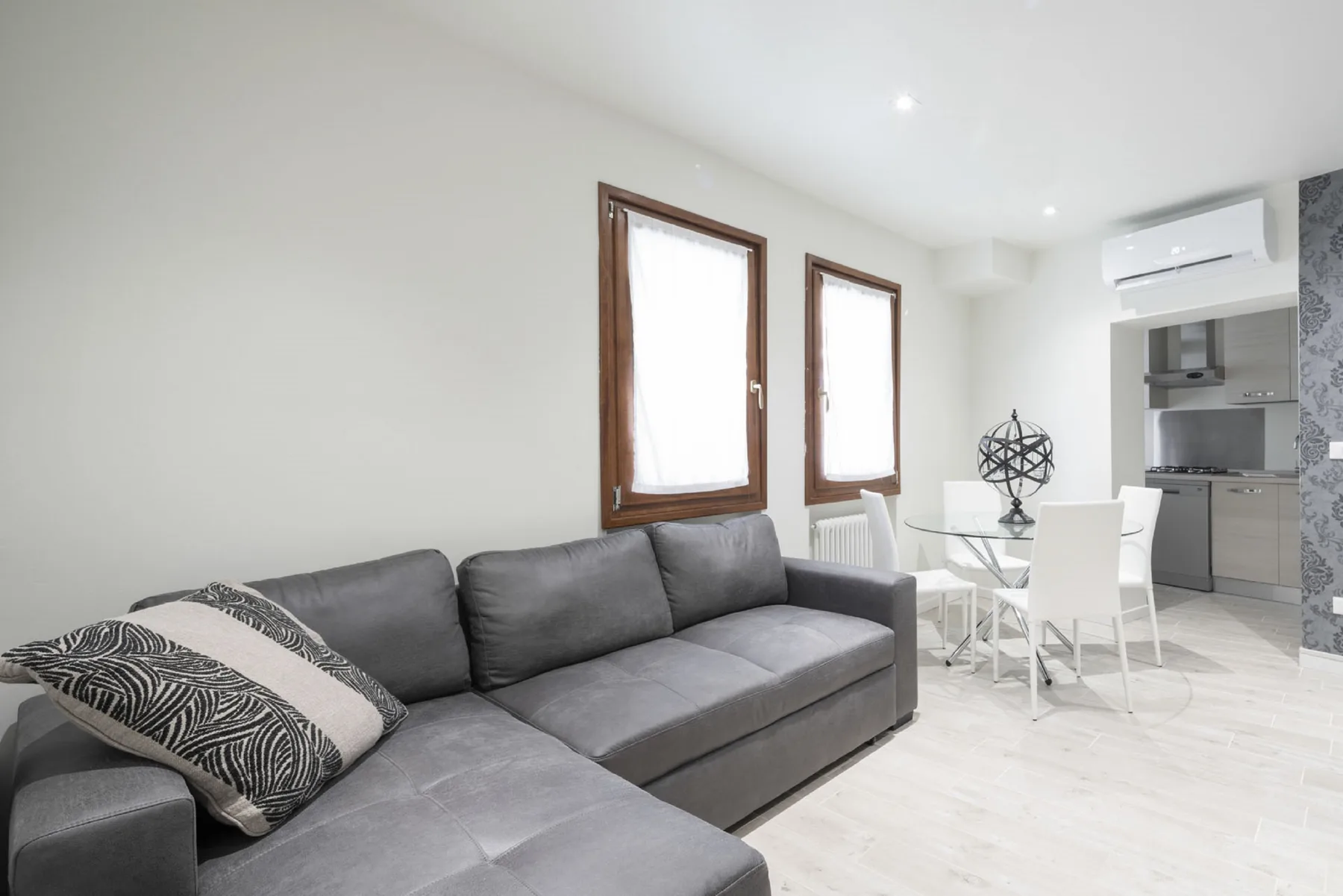 Sala de estar con asientos grises junto a una pequeña mesa de comedor y una cocina.
