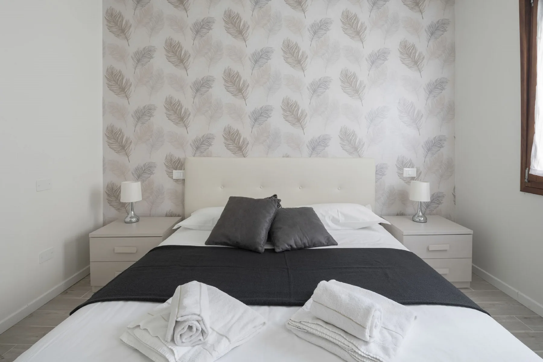 Un dormitorio con una cama bien tendida frente a una pared con motivos de hojas.