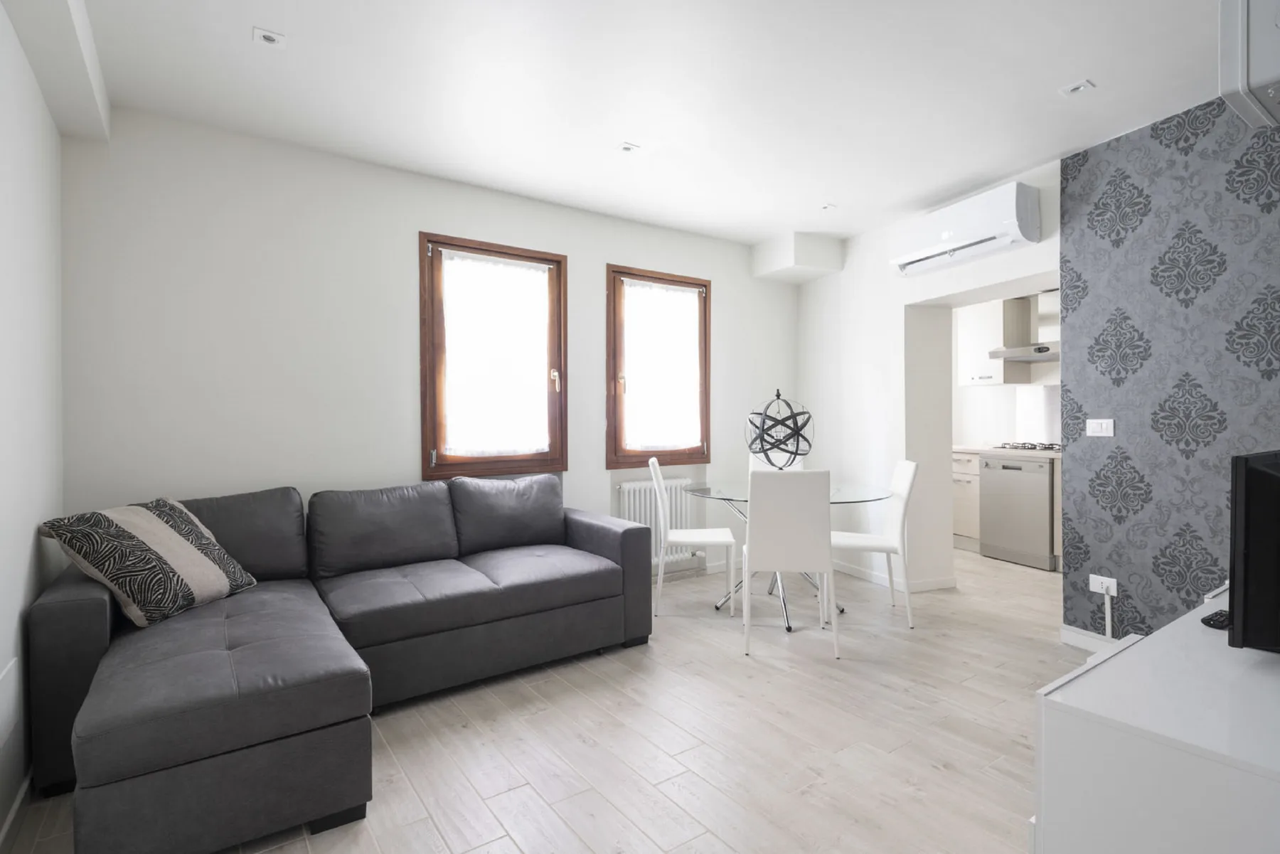 Una luminosa sala de estar y comedor con un sofá seccional gris y una mesa blanca.
