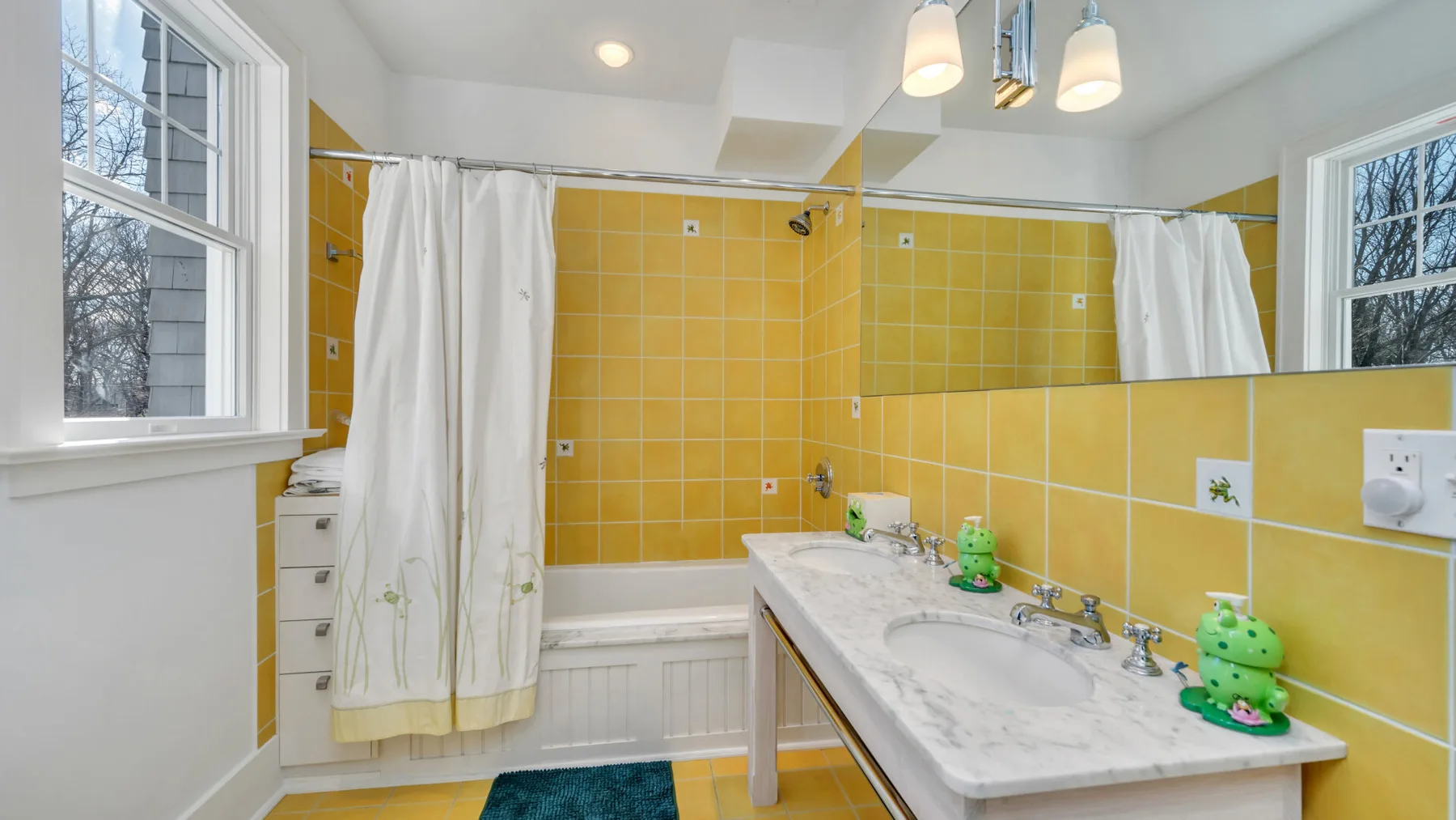 Un baño con una encimera larga con lavabo, azulejos amarillos y una bañera con cortina.
