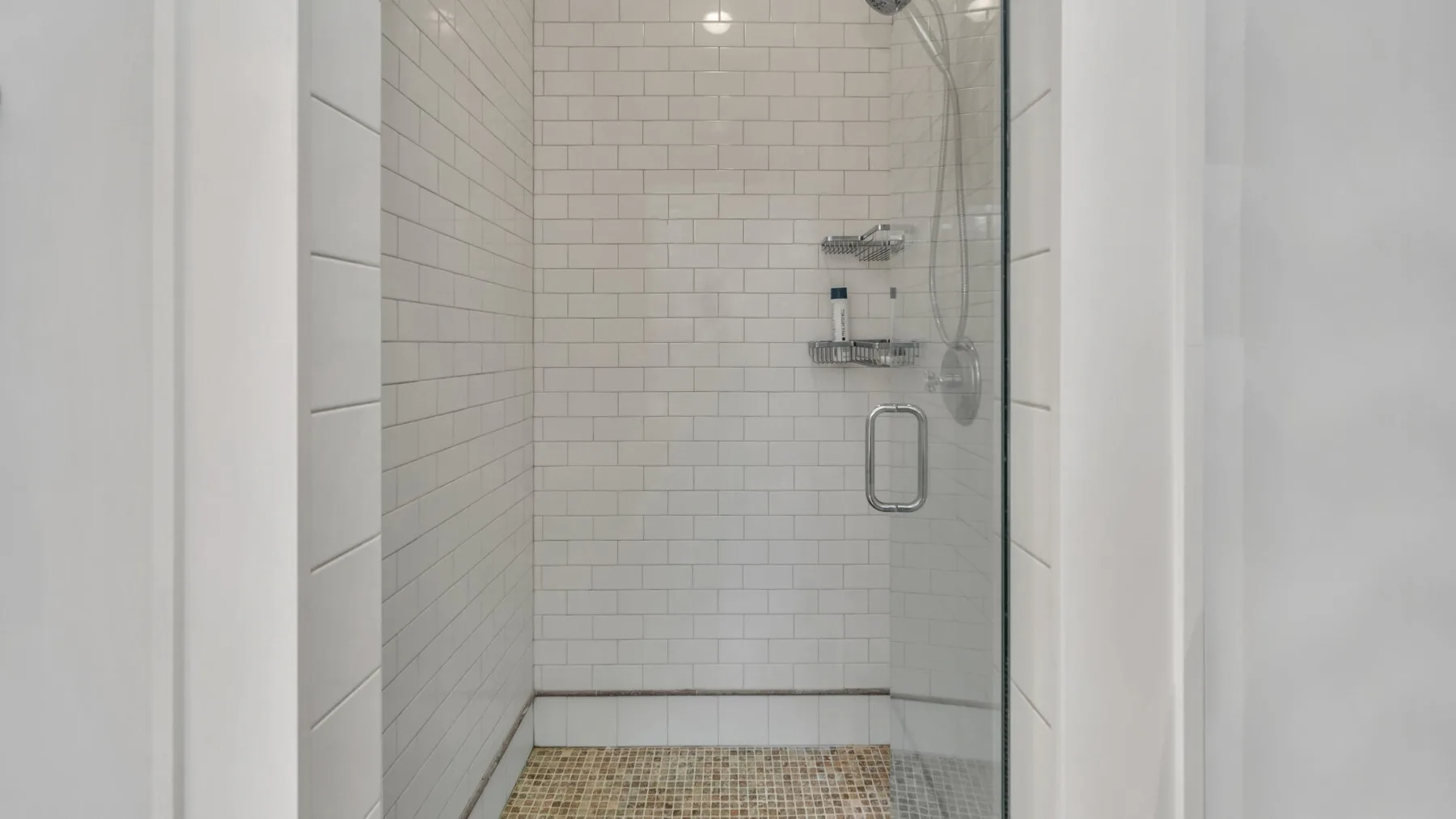 Una ducha con azulejos, un panel de vidrio y accesorios metálicos.