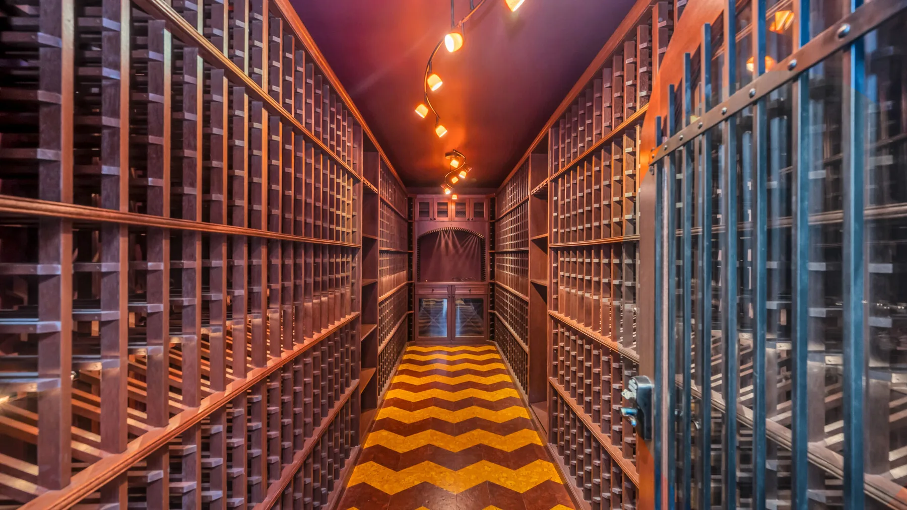 Una larga sala de almacenamiento de vino con filas de botellas y luces cálidas en el techo.