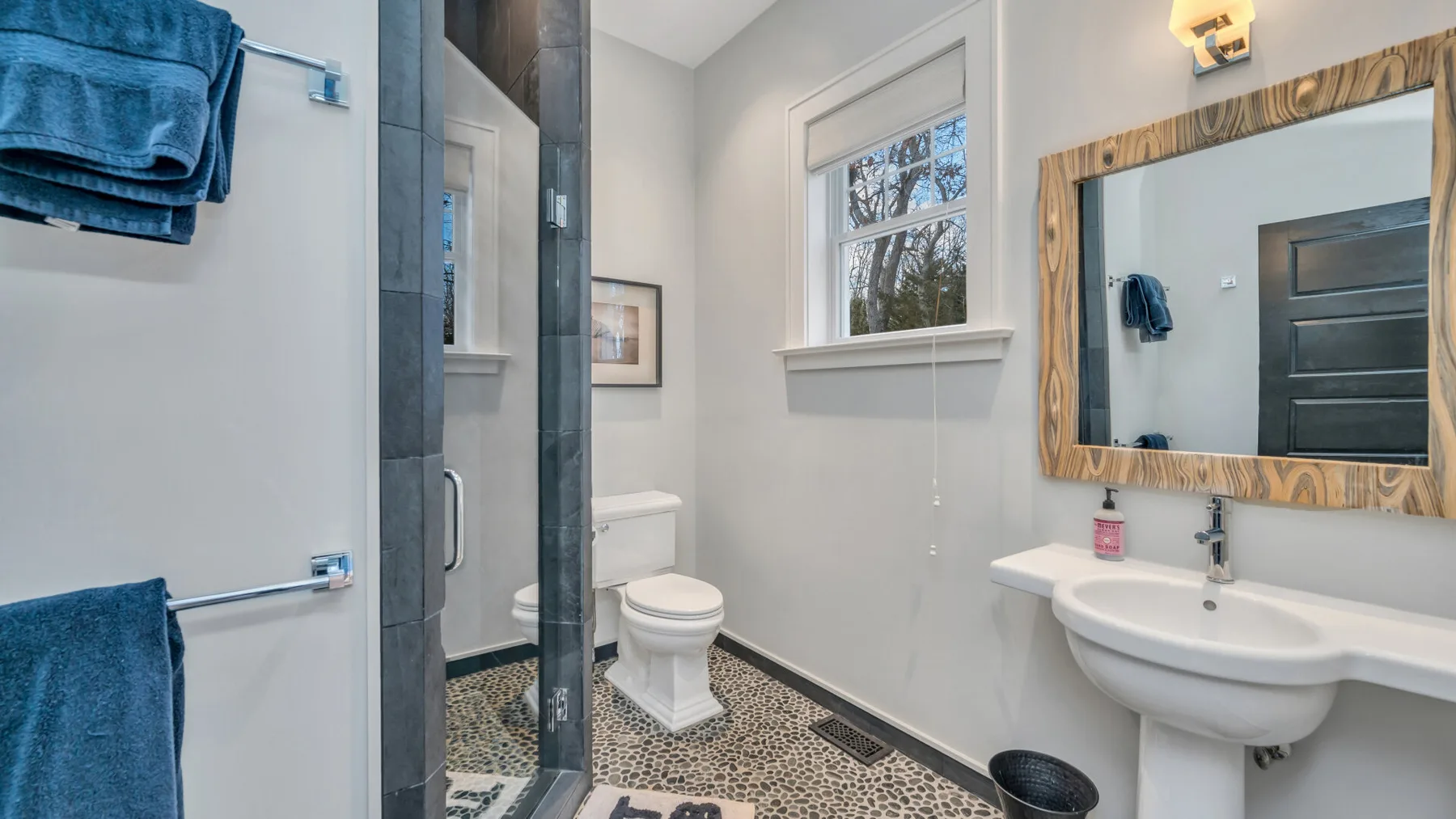 Un baño con ducha de vidrio, inodoro y lavabo bajo una ventana.