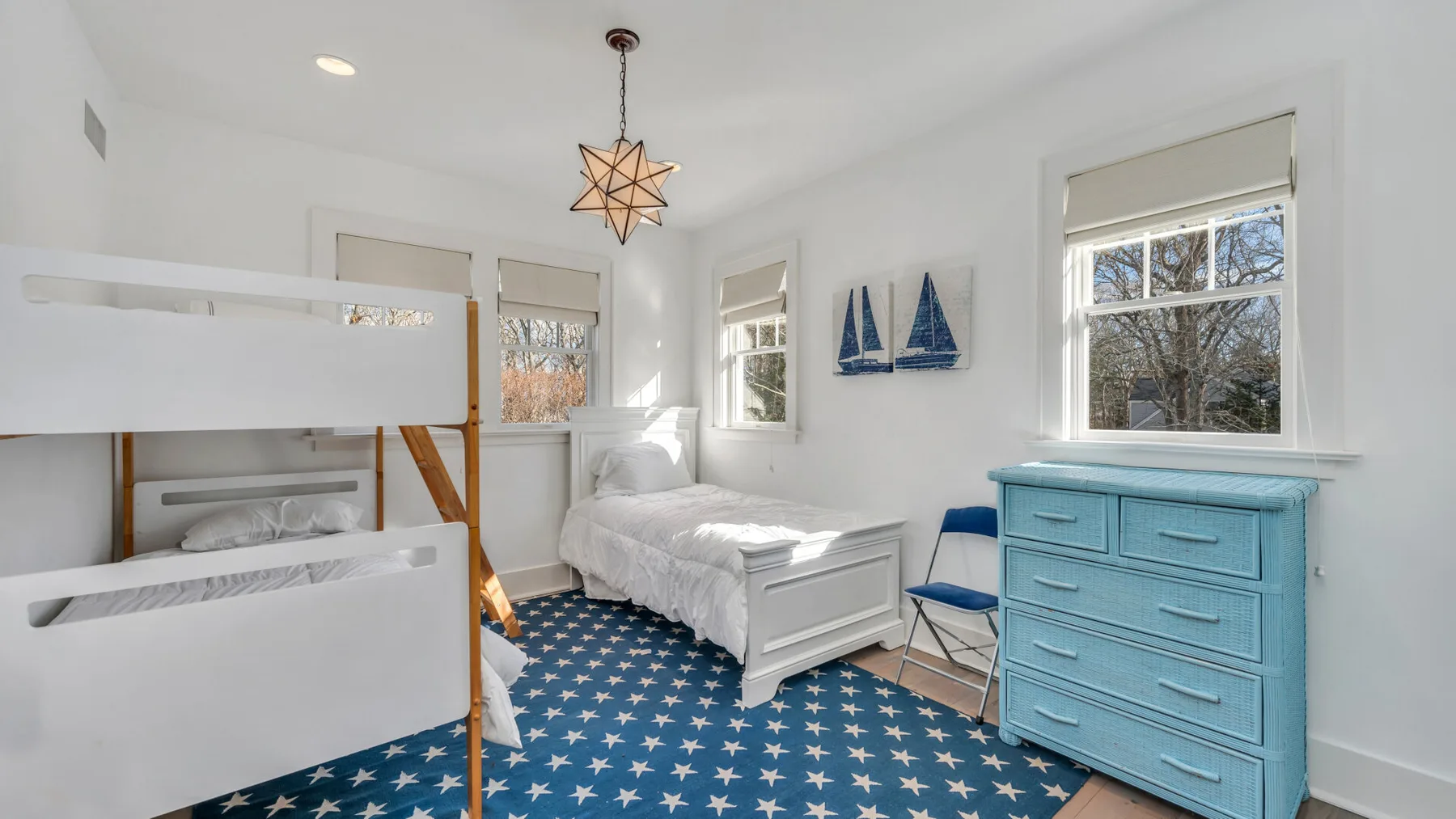 Un dormitorio luminoso con camas blancas, una cómoda azul y alfombra de estrellas.