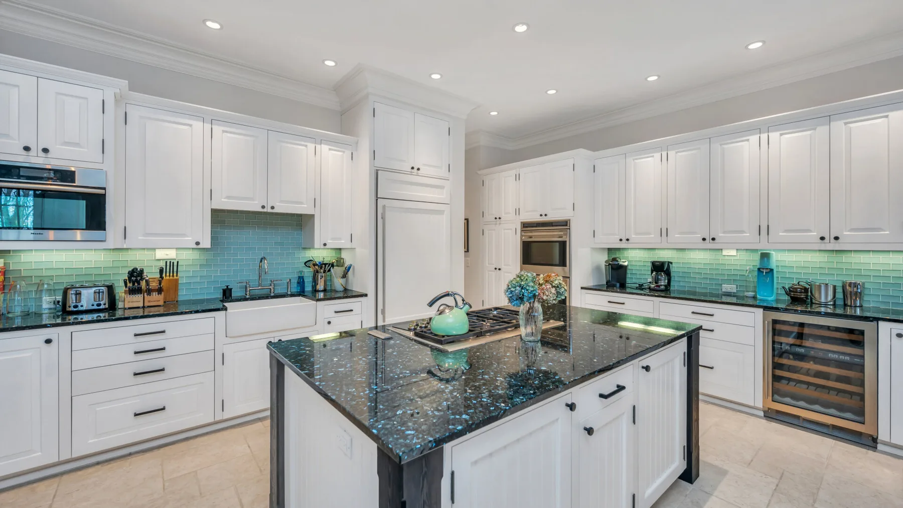 Una cocina luminosa con gabinetes blancos y una isla grande y oscura.