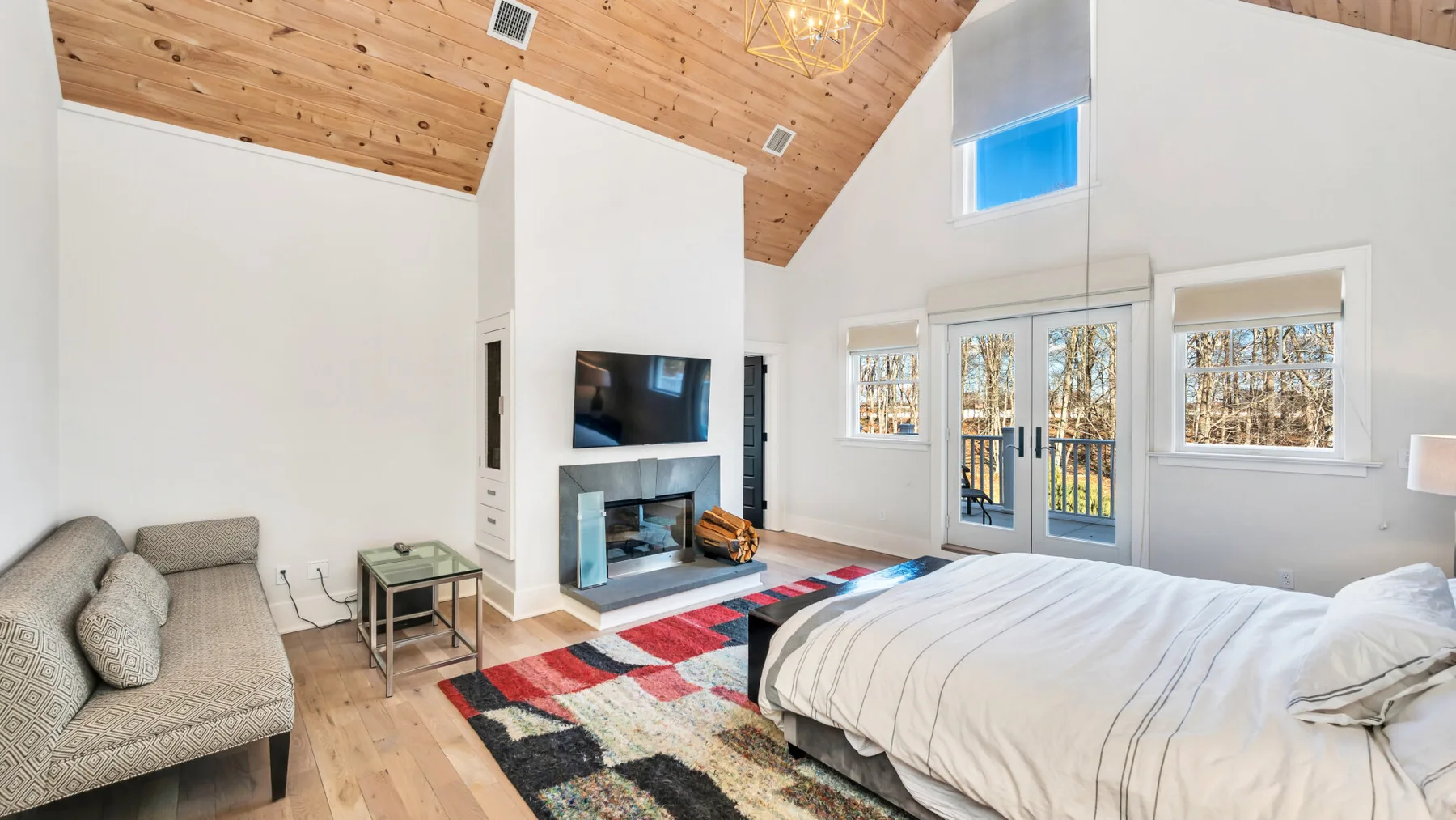 Un dormitorio luminoso con una cama grande, una chimenea y ventanas con vista a los árboles.