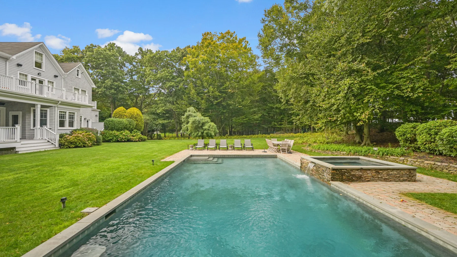 Una piscina al aire libre junto a un césped ajardinado y una casa grande.