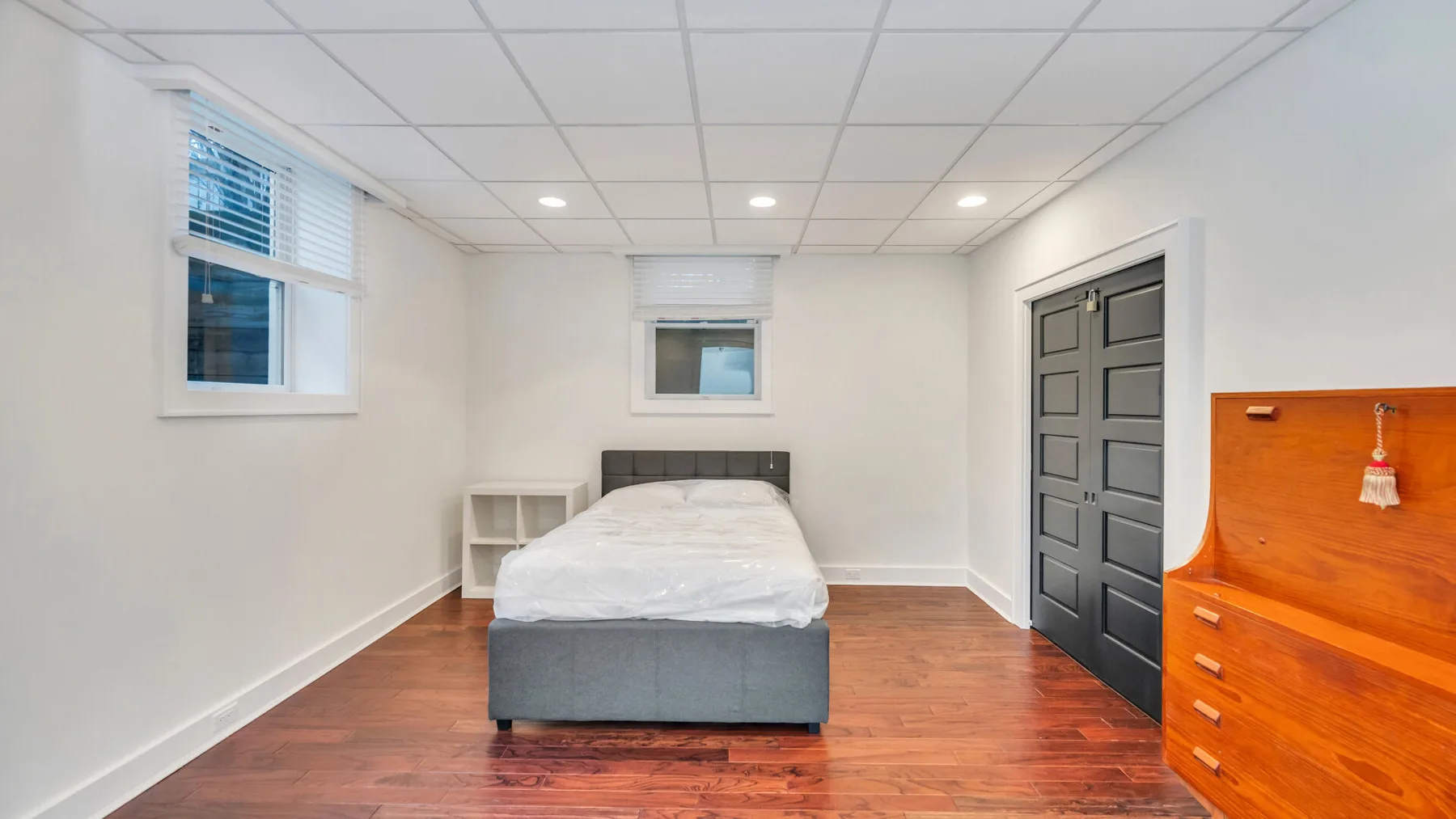 Un dormitorio con una cama, ventanas y una cómoda de madera.
