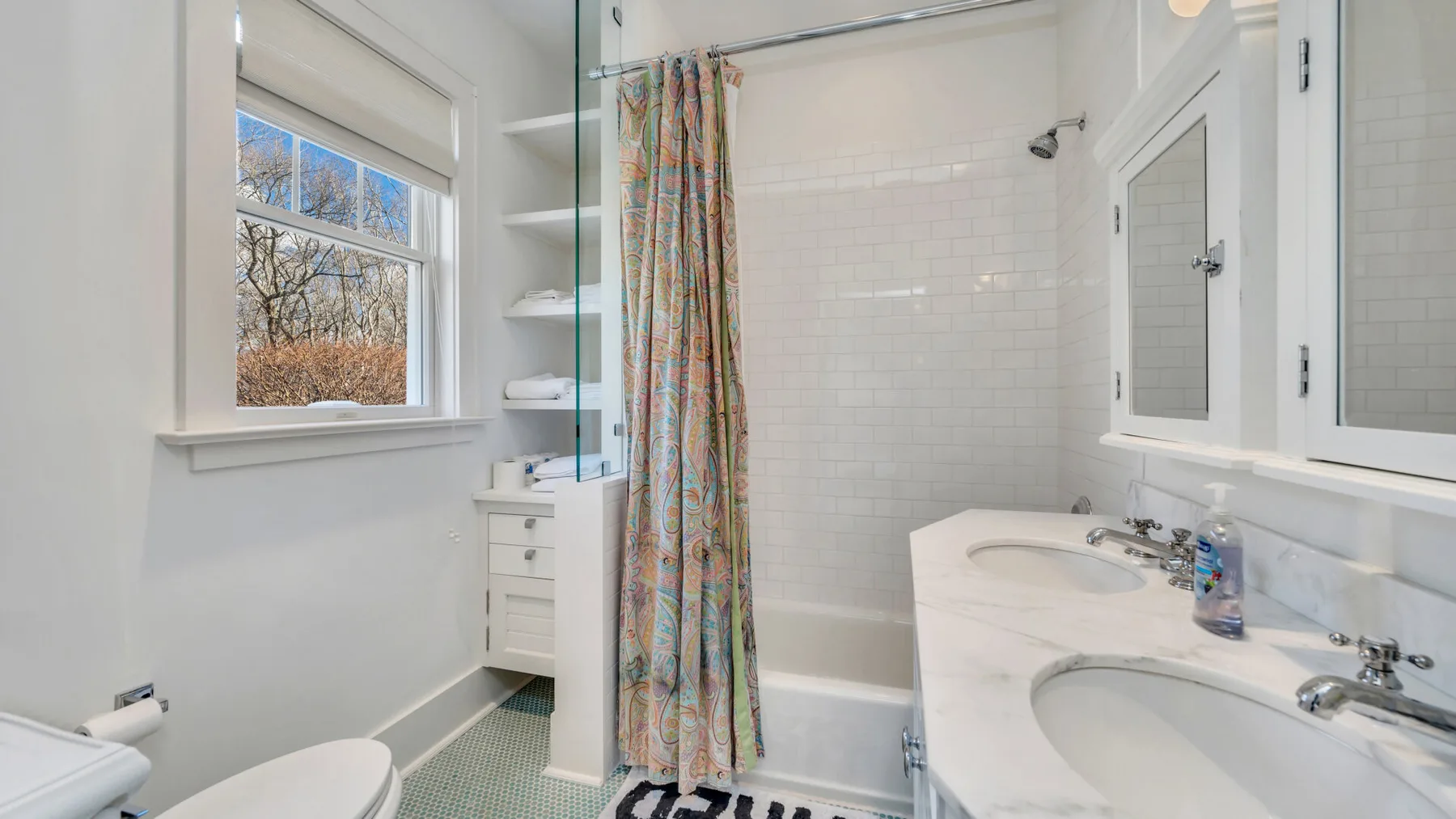 Un baño luminoso con bañera, cortina de ducha estampada y tocador con dos lavabos.