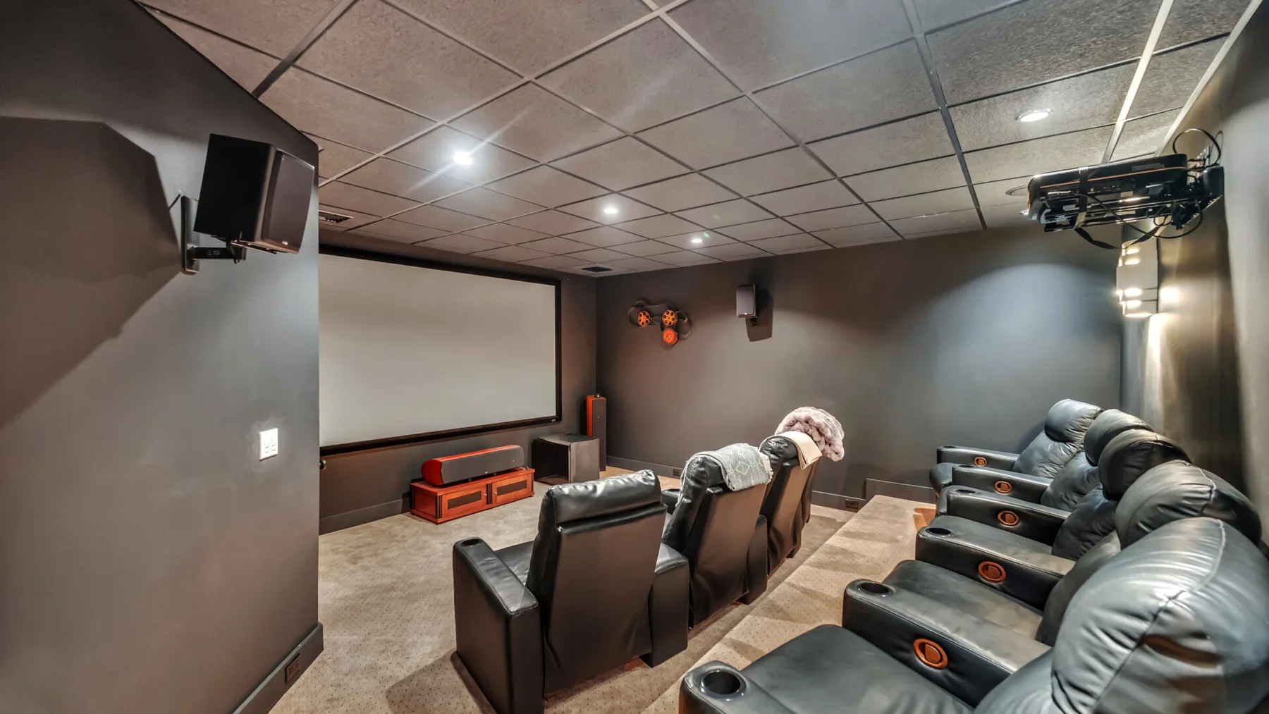 Una sala de cine en casa con filas de asientos reclinables frente a una pantalla grande.